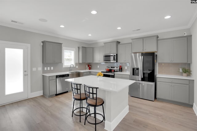 kitchen with appliances with stainless steel finishes, gray cabinets, a sink, a breakfast bar area, and light wood-style floors