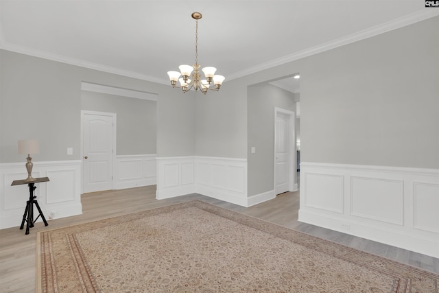 unfurnished dining area featuring light wood-type flooring, a chandelier, wainscoting, and crown molding