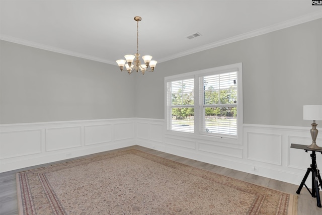 unfurnished dining area with a chandelier, a wainscoted wall, ornamental molding, wood finished floors, and a decorative wall