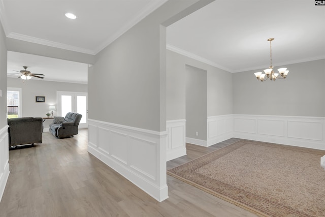 dining space featuring wainscoting, light wood finished floors, a chandelier, crown molding, and ceiling fan