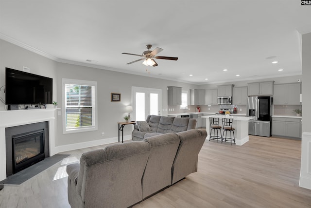 living room with ceiling fan, ornamental molding, a fireplace with flush hearth, light wood-style floors, and recessed lighting