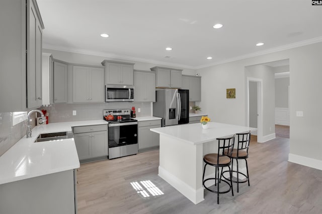 kitchen featuring appliances with stainless steel finishes, a sink, gray cabinets, a breakfast bar area, and ornamental molding