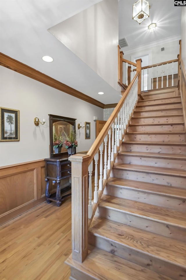 staircase featuring crown molding, wood finished floors, a wainscoted wall, and recessed lighting