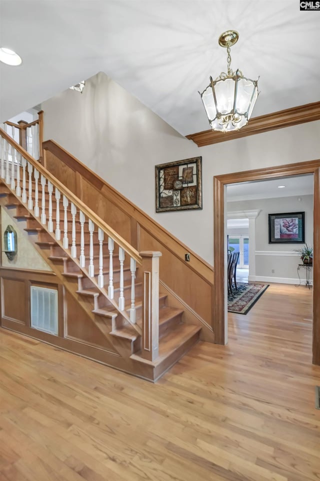 stairway with a chandelier, wood finished floors, ornamental molding, a wainscoted wall, and a decorative wall