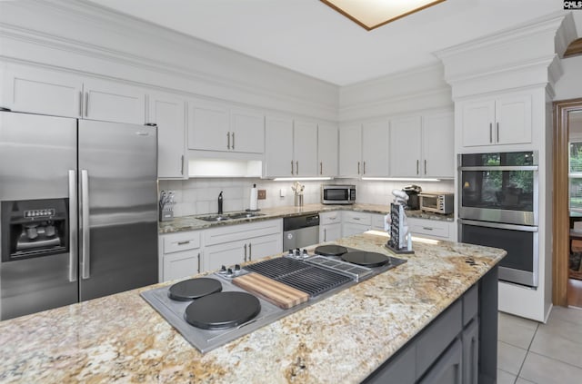 kitchen featuring appliances with stainless steel finishes, a sink, white cabinets, tasteful backsplash, and light tile patterned flooring