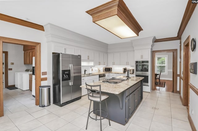 kitchen featuring stainless steel appliances, washing machine and clothes dryer, white cabinets, a kitchen island, and crown molding