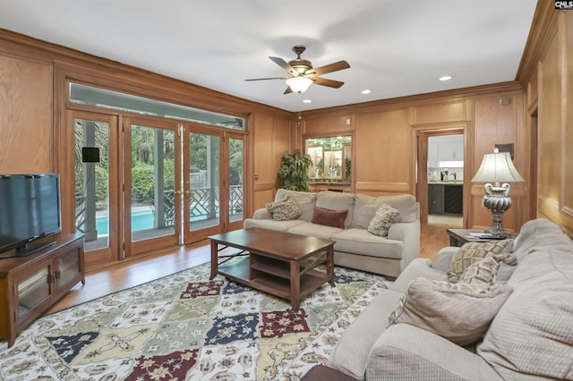 living room with a ceiling fan, light wood-type flooring, a decorative wall, and ornamental molding
