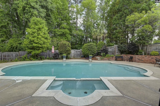 view of swimming pool featuring a patio, a fenced backyard, a pool with connected hot tub, and view of scattered trees