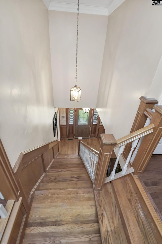 stairway featuring wood finished floors, a high ceiling, ornamental molding, and a chandelier