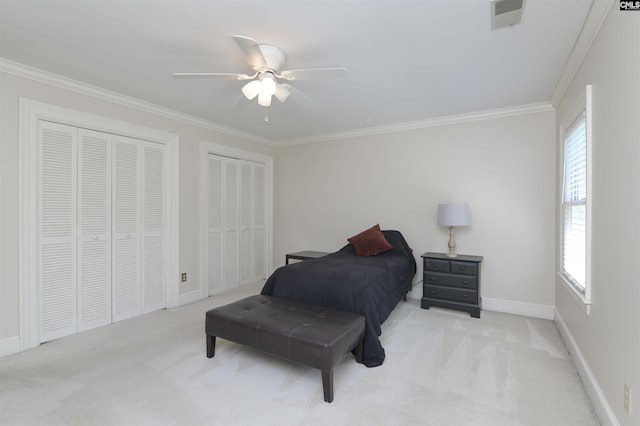 carpeted bedroom with two closets, ornamental molding, a ceiling fan, and baseboards