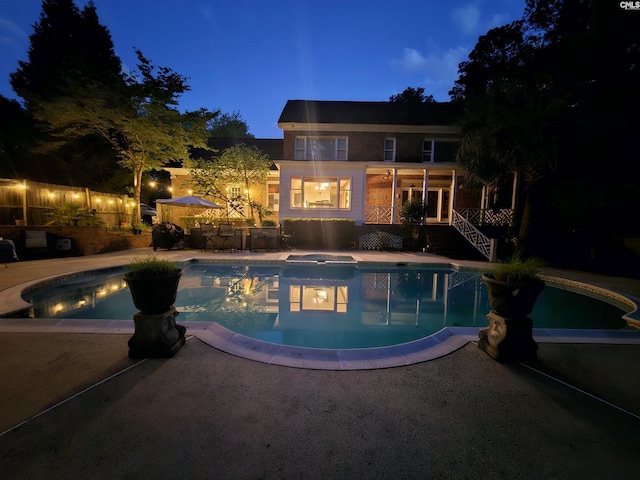 pool at night with a jacuzzi, an outdoor pool, and a patio area
