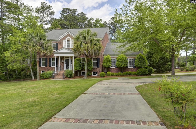 view of front facade featuring brick siding, a front yard, driveway, and covered porch