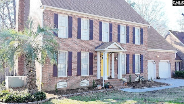 colonial-style house featuring brick siding, a shingled roof, a garage, and central AC unit