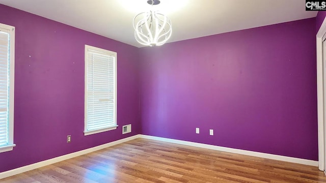 empty room featuring a chandelier, wood finished floors, and baseboards