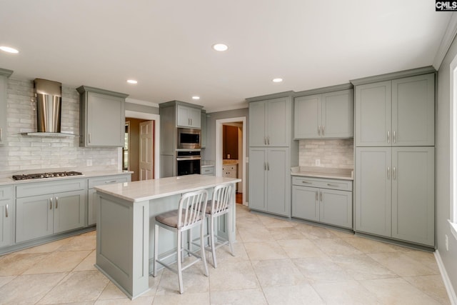 kitchen with appliances with stainless steel finishes, wall chimney exhaust hood, gray cabinetry, backsplash, and ornamental molding