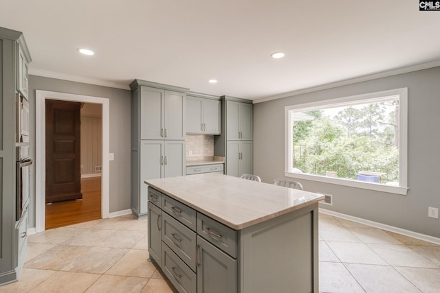 kitchen with gray cabinets, ornamental molding, light stone counters, baseboards, and a kitchen island