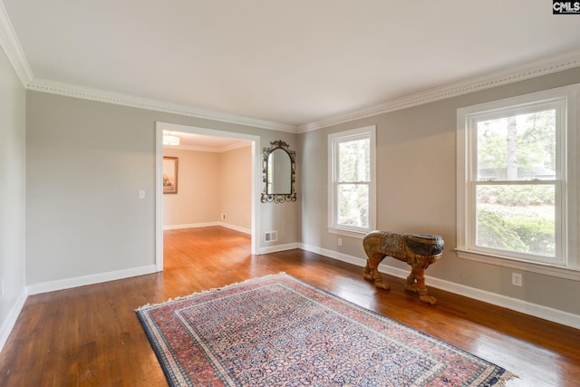 empty room featuring wood finished floors, ornamental molding, and baseboards