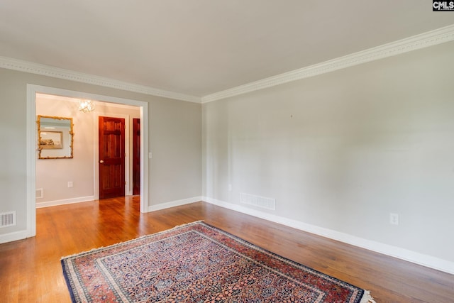 spare room featuring wood finished floors, crown molding, and baseboards
