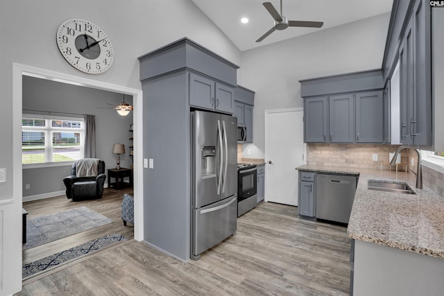 kitchen featuring stainless steel appliances, ceiling fan, a sink, high vaulted ceiling, and light stone countertops