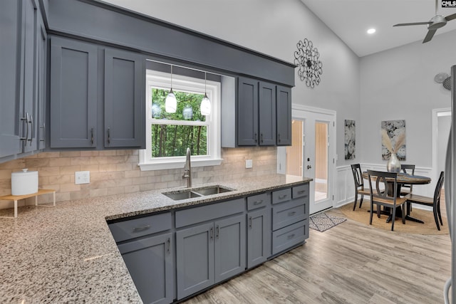 kitchen featuring a sink, a high ceiling, backsplash, light stone counters, and light wood-style floors