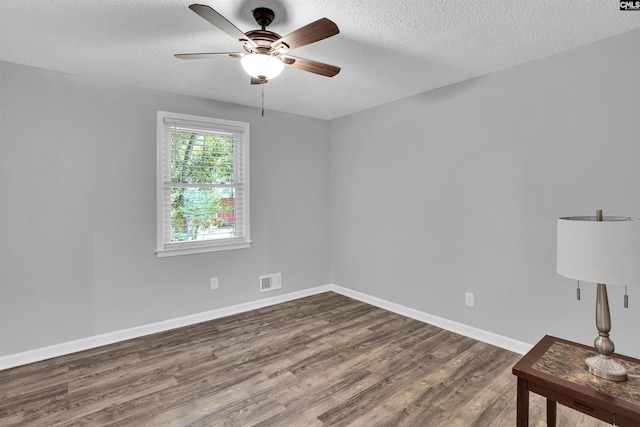 empty room featuring dark wood-type flooring, a ceiling fan, a textured ceiling, and baseboards