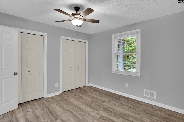 unfurnished bedroom featuring multiple closets, wood finished floors, baseboards, and a textured ceiling