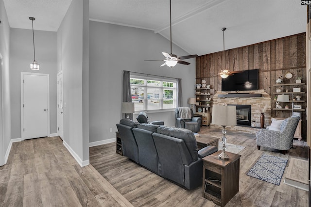 living area featuring a glass covered fireplace, ceiling fan, wood finished floors, baseboards, and high vaulted ceiling