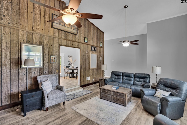 living area featuring a high ceiling, ceiling fan, wooden walls, and wood finished floors