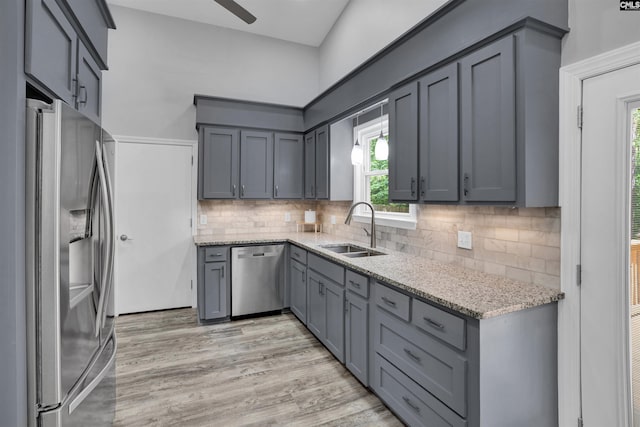 kitchen featuring stainless steel appliances, a sink, gray cabinets, and light stone countertops