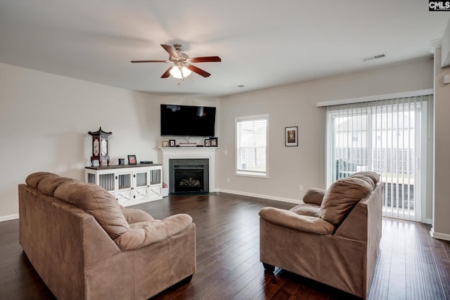 living room featuring a ceiling fan, a fireplace with flush hearth, baseboards, and dark wood-type flooring