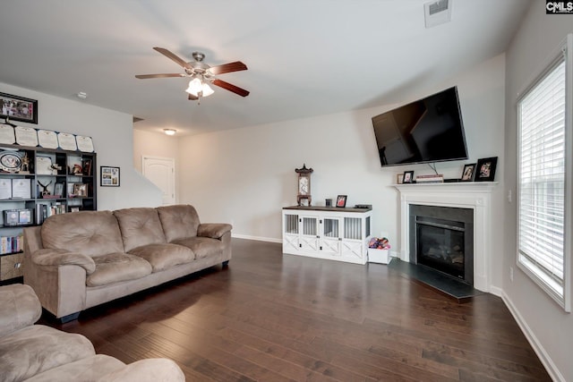 living area with ceiling fan, plenty of natural light, a glass covered fireplace, and wood finished floors