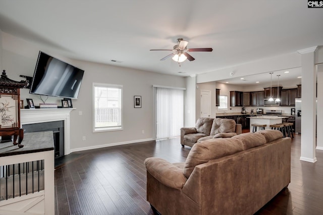 living room with a ceiling fan, baseboards, dark wood-type flooring, a glass covered fireplace, and recessed lighting