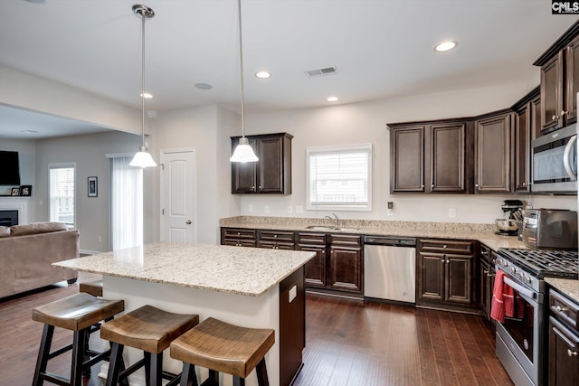 kitchen featuring stainless steel appliances, open floor plan, dark brown cabinets, a sink, and a kitchen breakfast bar