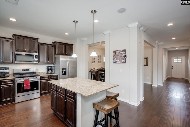 kitchen with appliances with stainless steel finishes, a kitchen bar, dark brown cabinetry, dark wood-style flooring, and recessed lighting