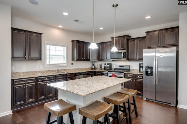 kitchen with stainless steel appliances, a sink, dark brown cabinets, a breakfast bar, and a center island