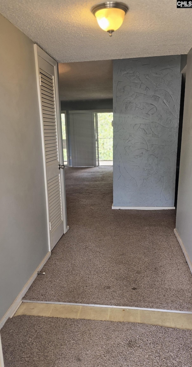 hall with carpet flooring, a textured ceiling, and baseboards