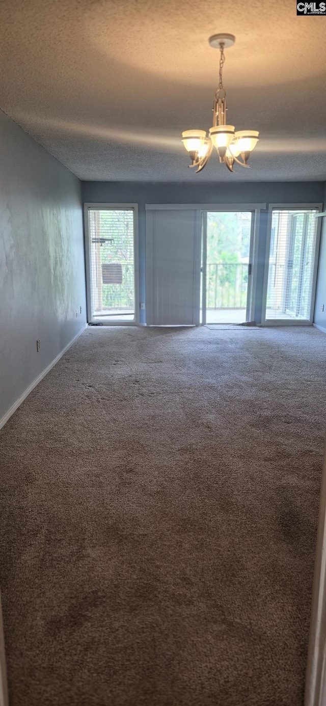 empty room featuring carpet flooring, a chandelier, a textured ceiling, and baseboards
