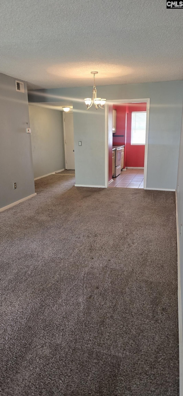 empty room with a chandelier, light carpet, and a textured ceiling