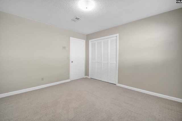 unfurnished bedroom featuring a closet, light carpet, a textured ceiling, and baseboards