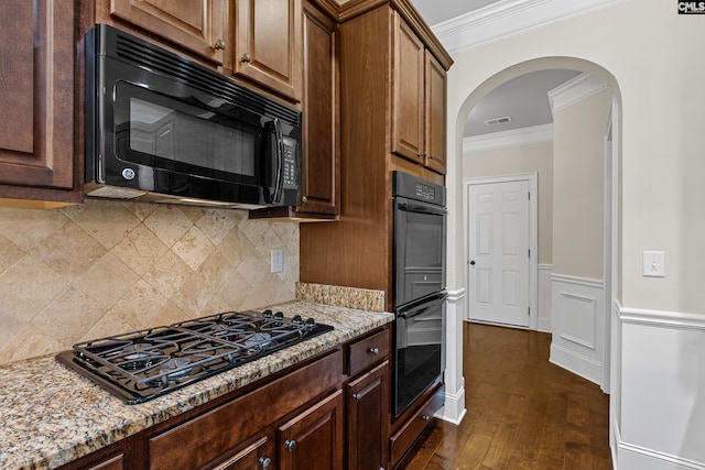 kitchen featuring black appliances, crown molding, arched walkways, light stone counters, and decorative backsplash