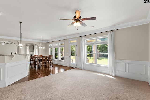 dining room with dark carpet, crown molding, a ceiling fan, healthy amount of natural light, and a decorative wall