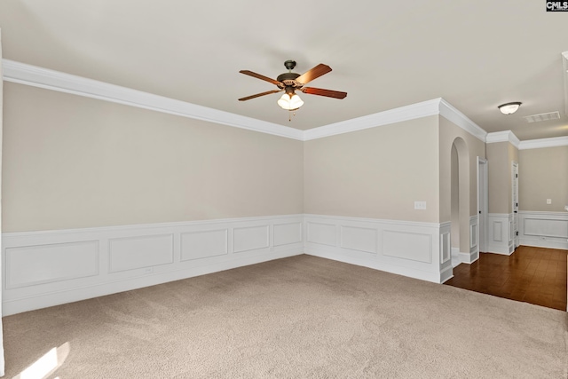 unfurnished room featuring carpet flooring, arched walkways, ceiling fan, ornamental molding, and a wainscoted wall