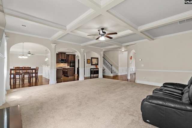 carpeted living area with arched walkways, ornate columns, ceiling fan, coffered ceiling, and crown molding