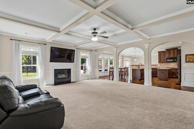 living room with arched walkways, coffered ceiling, a ceiling fan, beam ceiling, and a fireplace with flush hearth