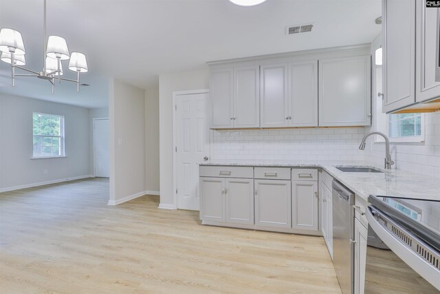kitchen featuring dishwasher, a sink, backsplash, and a chandelier