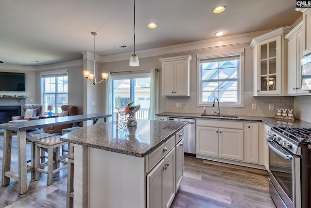 kitchen featuring a sink, stainless steel appliances, open floor plan, crown molding, and healthy amount of natural light