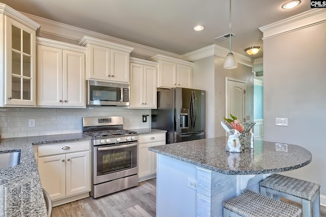 kitchen featuring appliances with stainless steel finishes, light wood-style flooring, a breakfast bar area, dark stone countertops, and ornamental molding