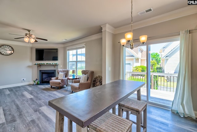 dining space with ornamental molding, a glass covered fireplace, wood finished floors, a chandelier, and baseboards
