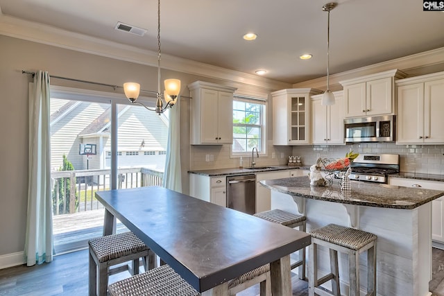 kitchen featuring appliances with stainless steel finishes, a sink, crown molding, decorative backsplash, and glass insert cabinets