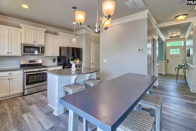 kitchen featuring stainless steel appliances, a kitchen island, wood finished floors, tasteful backsplash, and crown molding
